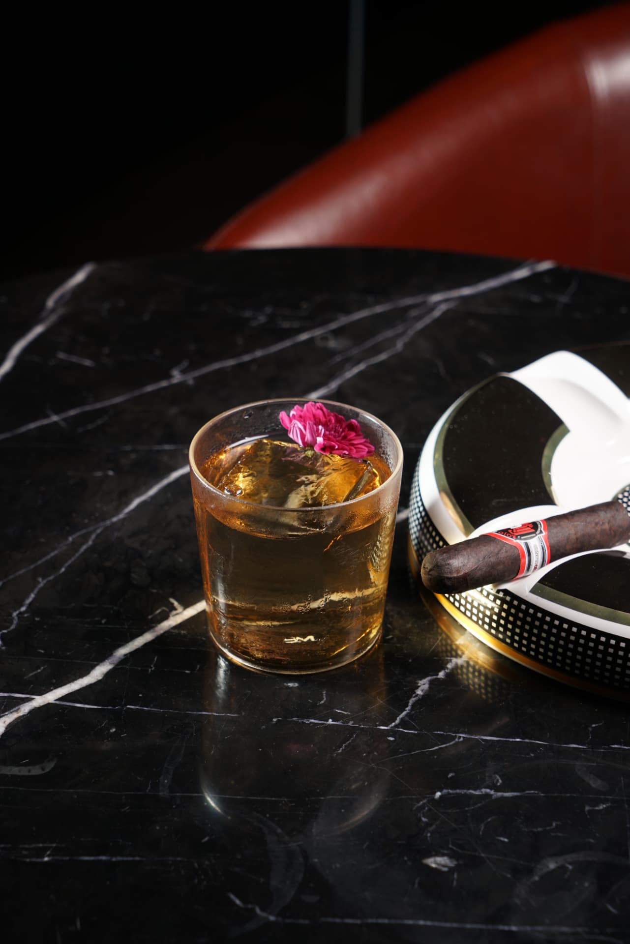 Whisky on a large ice cube beside a cigar and ashtray