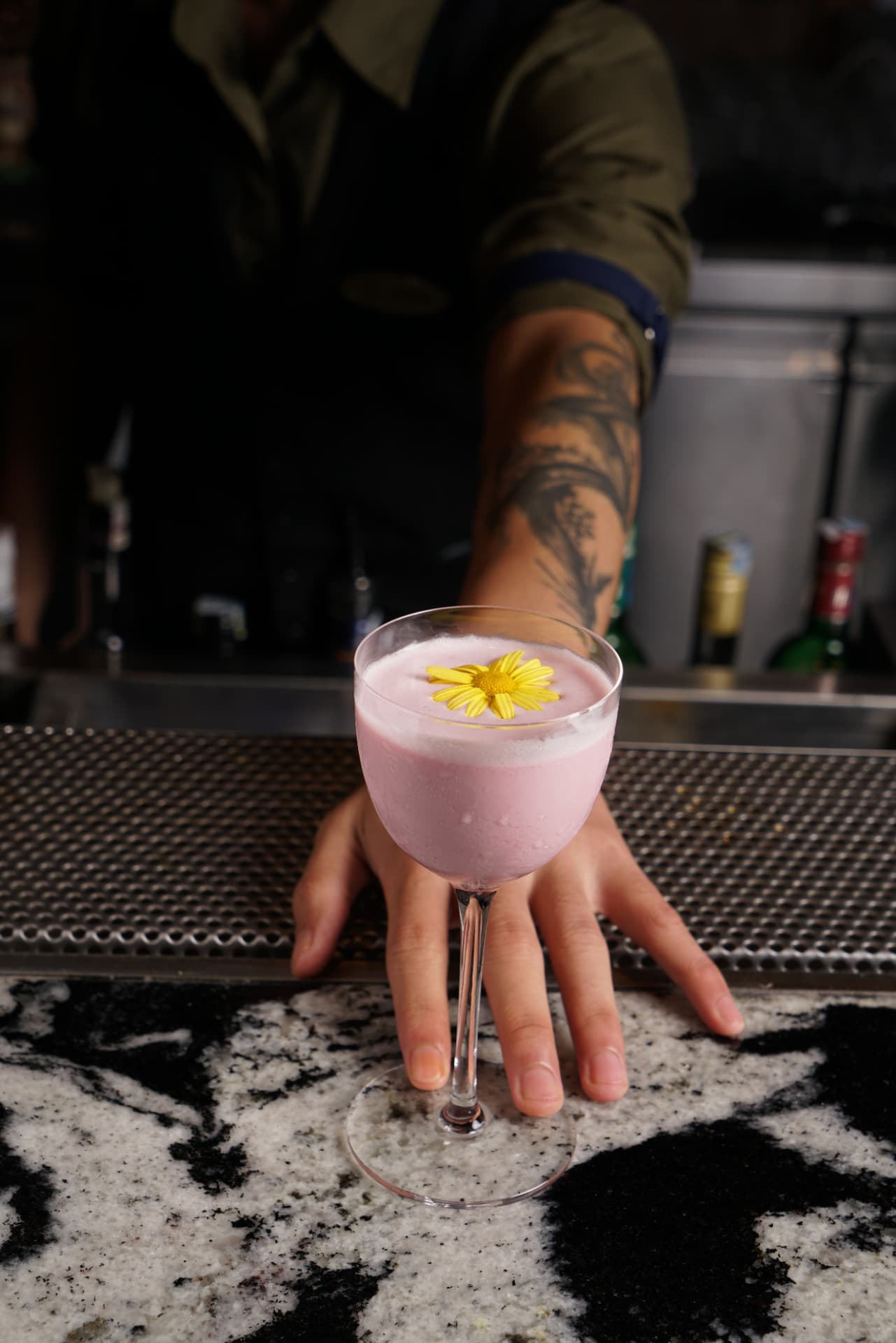 Pink foamed signature cocktail with a yellow flower garnish