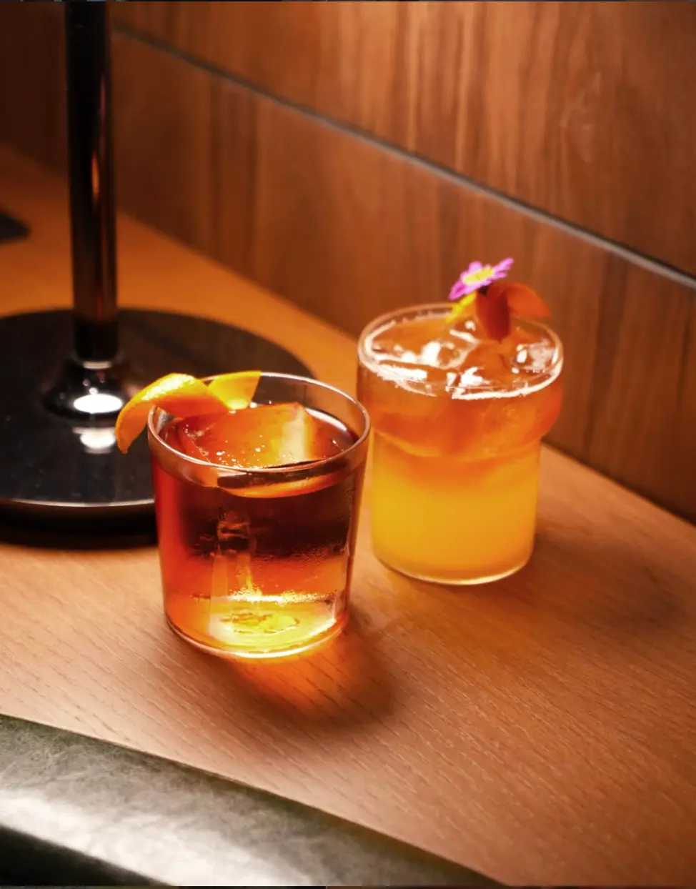 Two cocktails on a warm lit wooden bar top