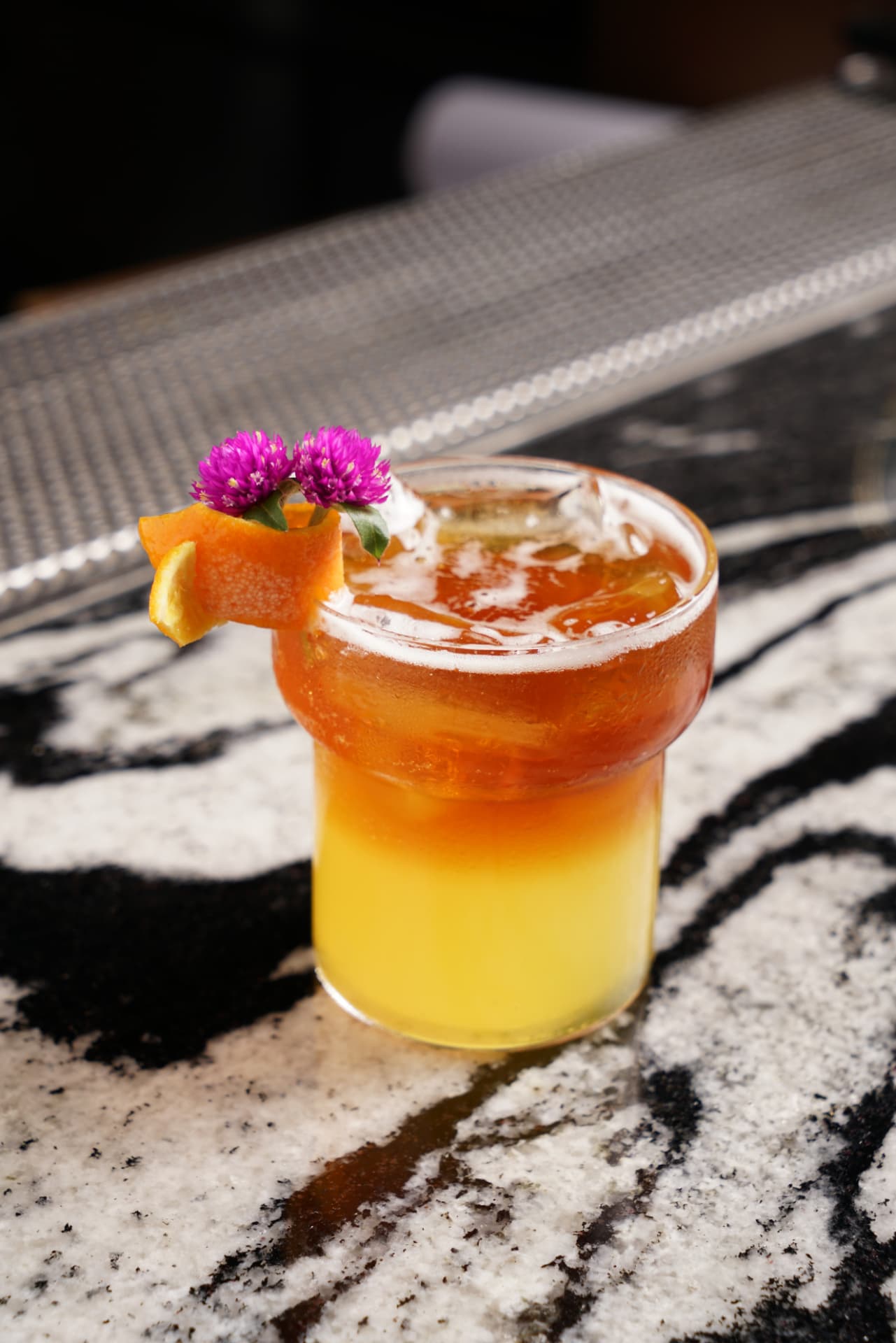 Layered orange cocktail with citrus peel and flowers